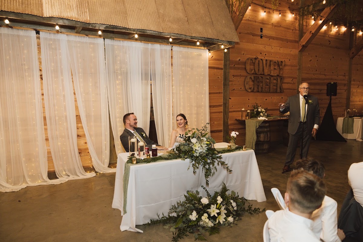 Emily & Bryan laugh at their sweetheart table during a toast in the wood-paneled indoor reception at Covey Creek.