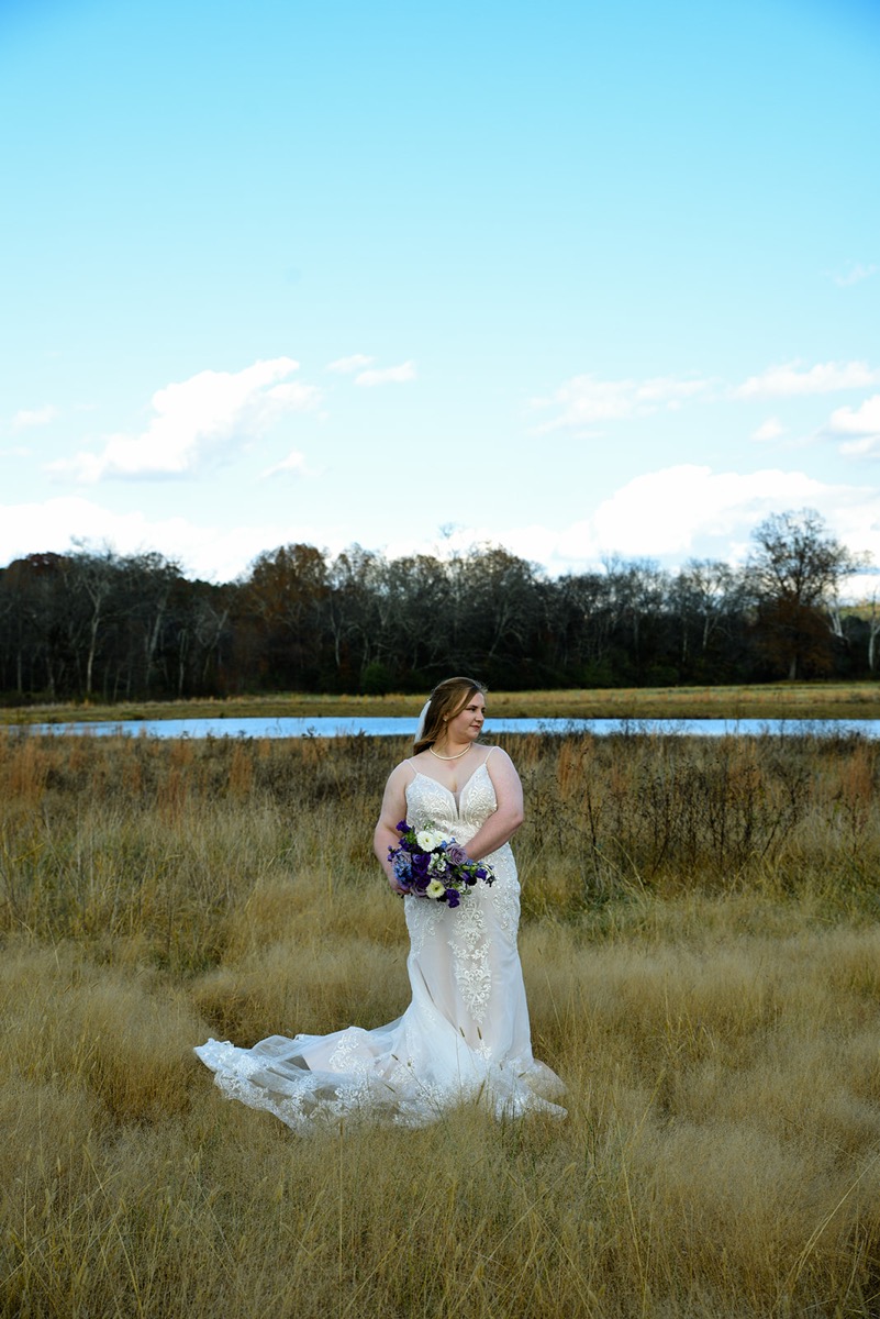 Emily stands in tall golden grass by the Pond in her lace gown for Emily & Jared's portraits at Covey Creek.