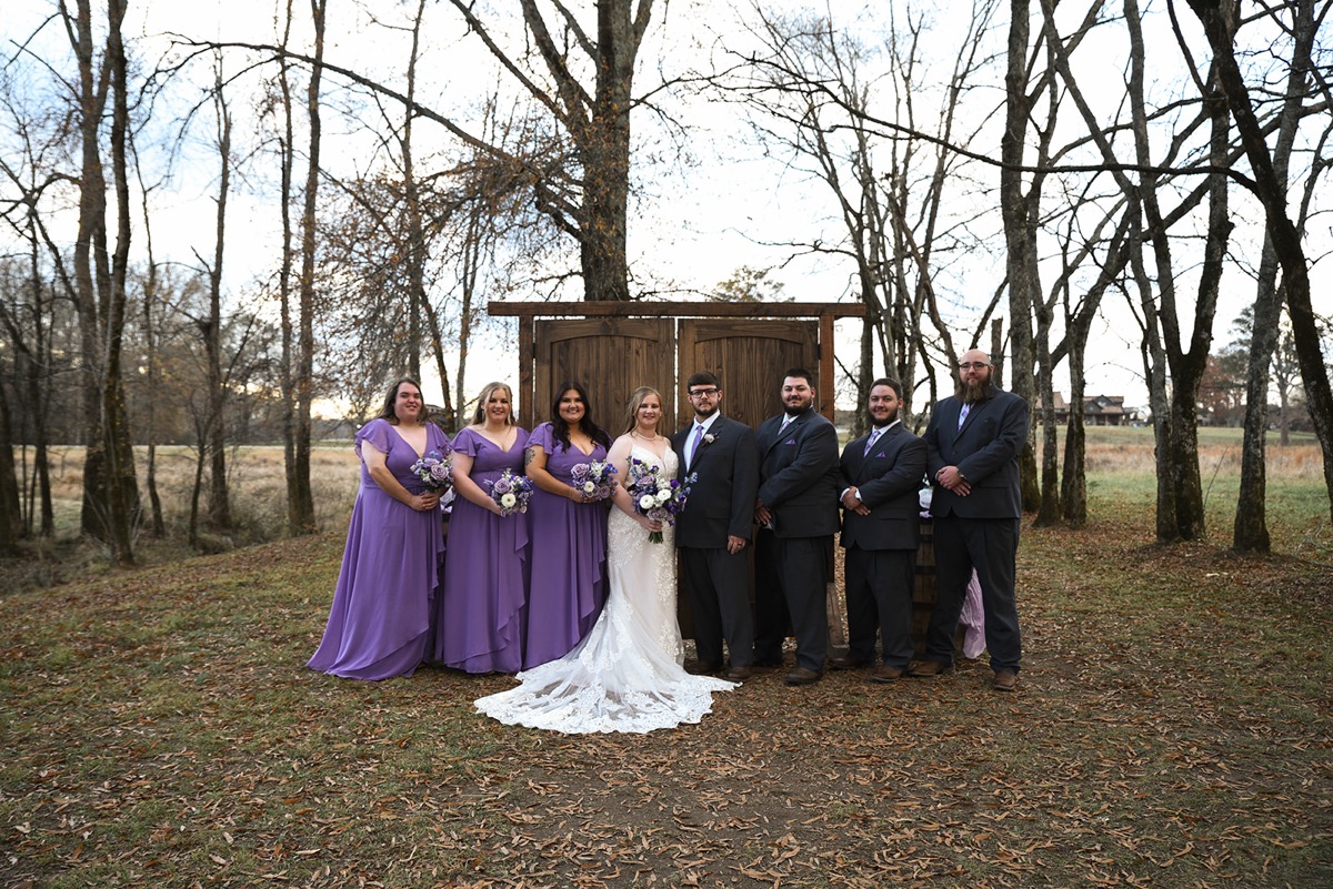 Emily & Jared stand centered with their wedding party in lavender and charcoal outside at Covey Creek.
