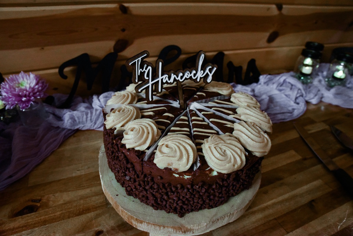 A chocolate chip cake with The Hancocks topper marks Emily & Jared's dessert table indoors at Covey Creek.