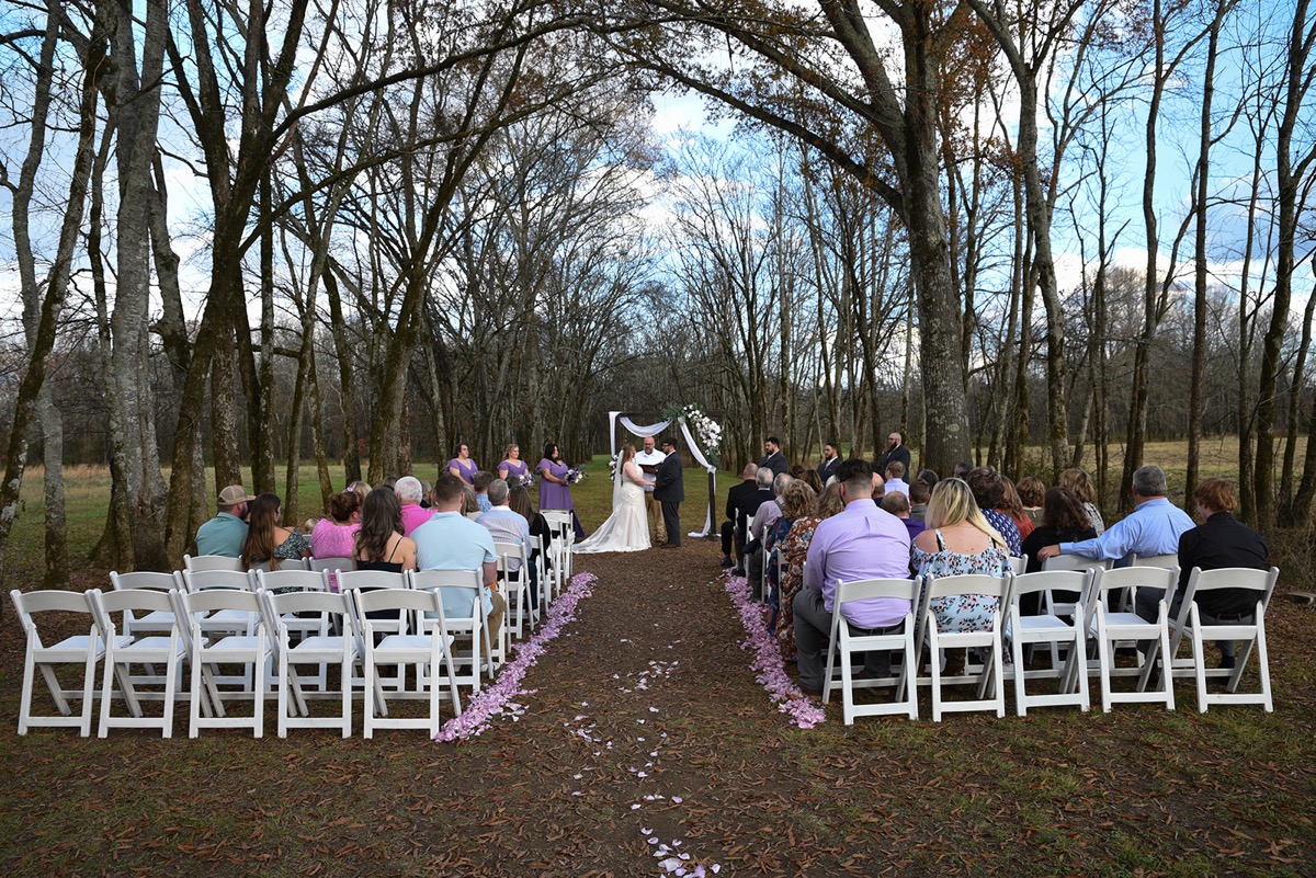 Guests face Emily & Jared at a flowered arbor along a petal aisle in the wooded ceremony at Covey Creek.