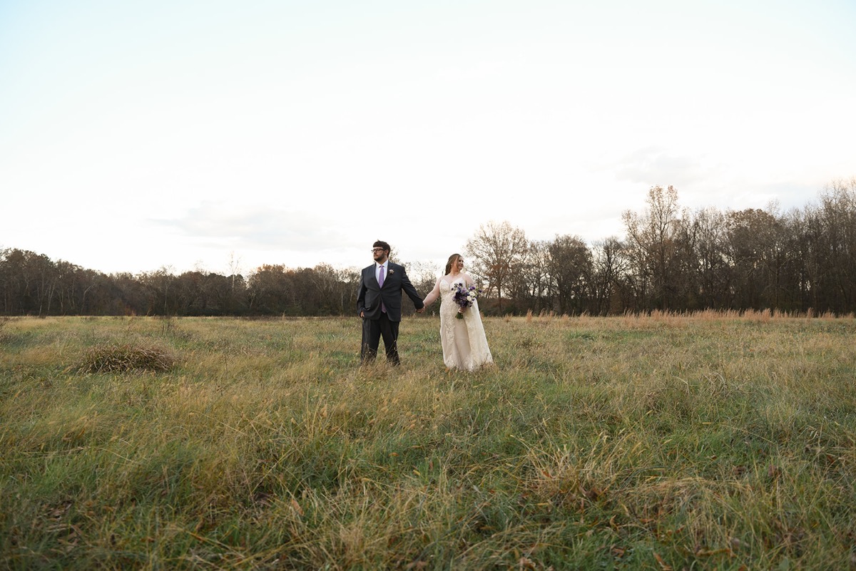 Emily & Jared hold hands in a wide grassy field under bare trees during fall portraits at Covey Creek.