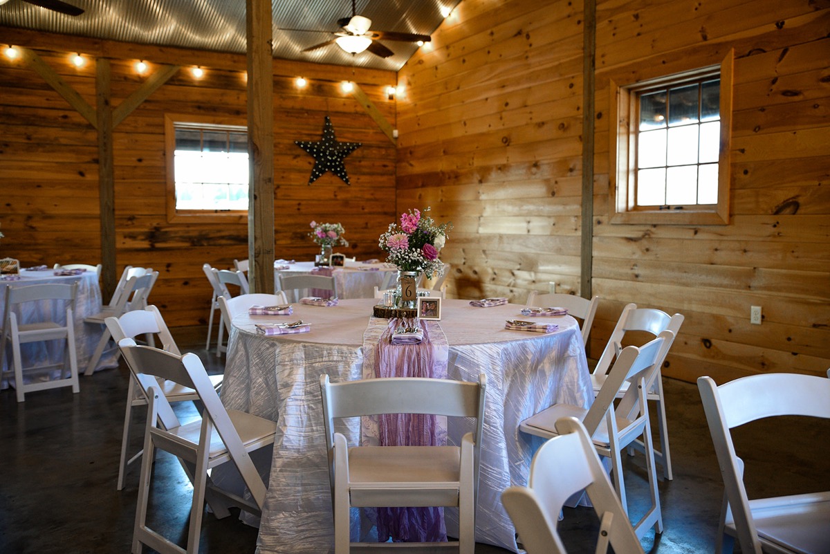 Round tables with purple runners and mason-jar florals fill Emily & Jared's barn reception hall at Covey Creek.