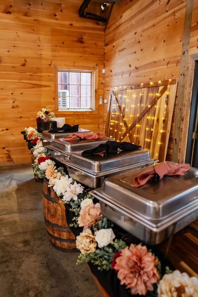 Erica & Randall buffet on a barrel-based table with floral garland and fairy-lit barn door at Covey Creek