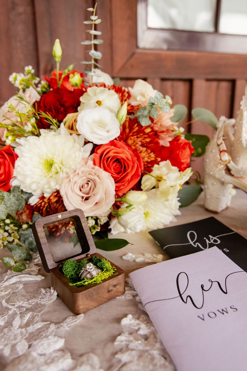 Erica & Randall wedding rings in a moss-lined box beside vow books and red florals at Covey Creek