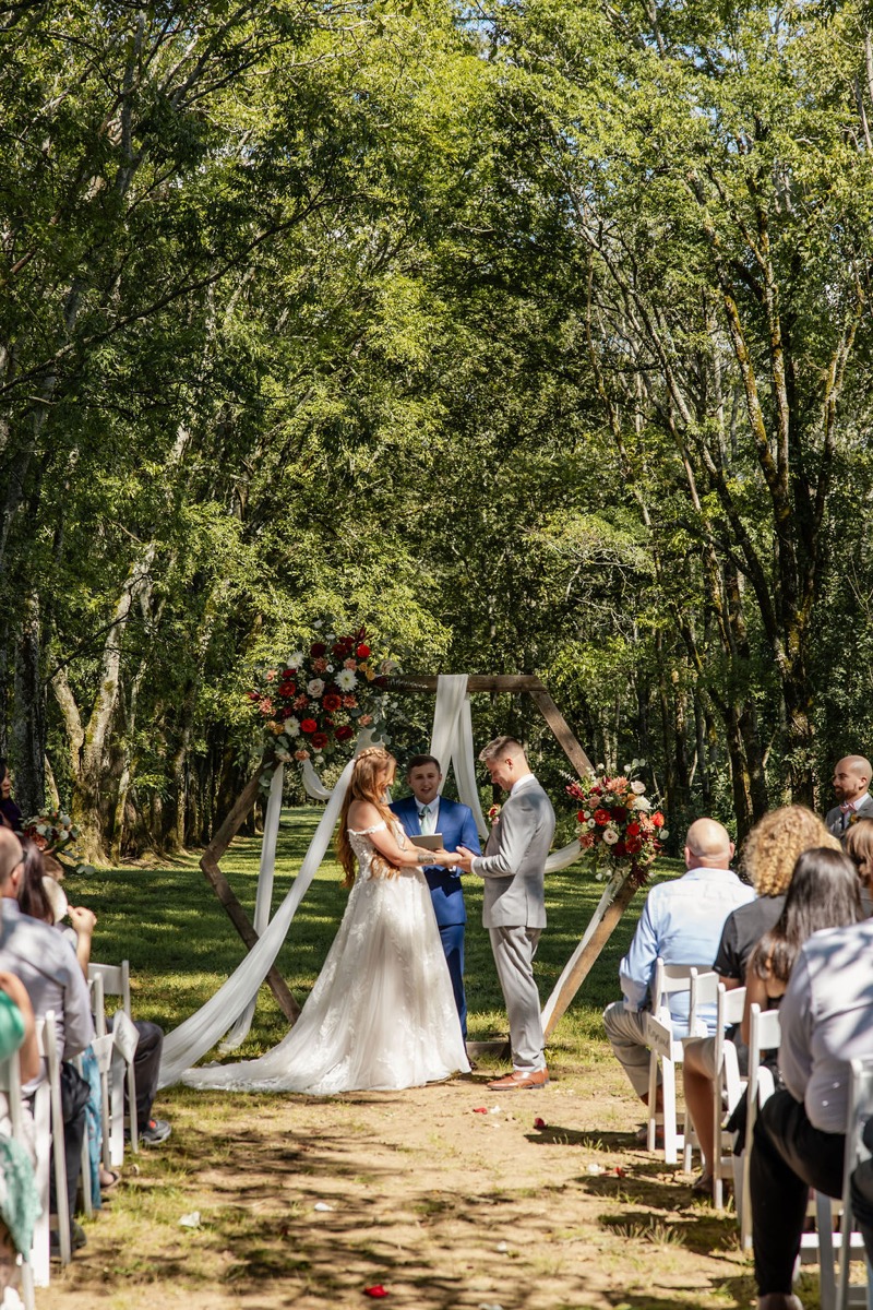 Erica & Randall exchange vows under a floral hexagonal arbor as guests watch at Covey Creek Tunnel of Love