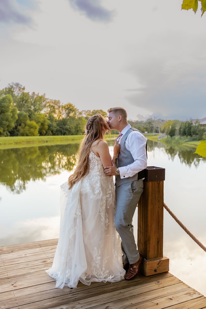 Erica & Randall kiss on the wooden dock above the still pond reflecting trees at Covey Creek’s Pond