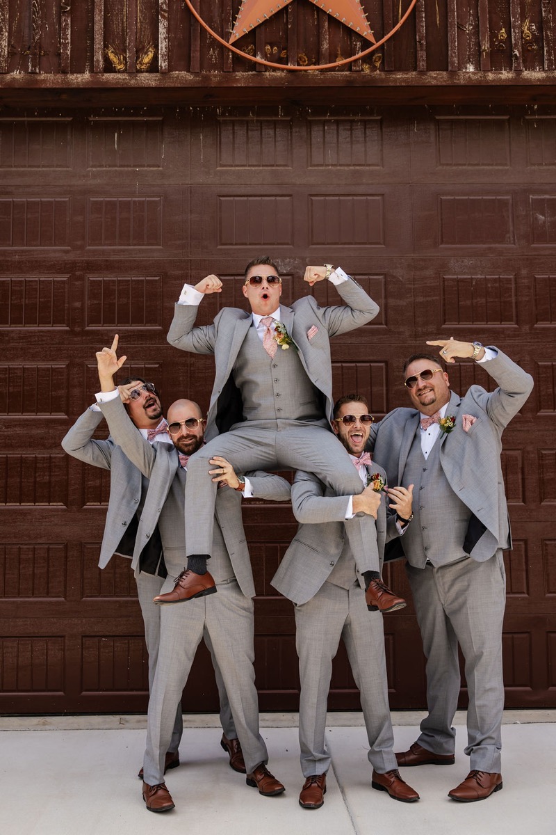 Erica & Randall’s groom sits on groomsmen’s shoulders in grey suits before the Covey Creek barn star door