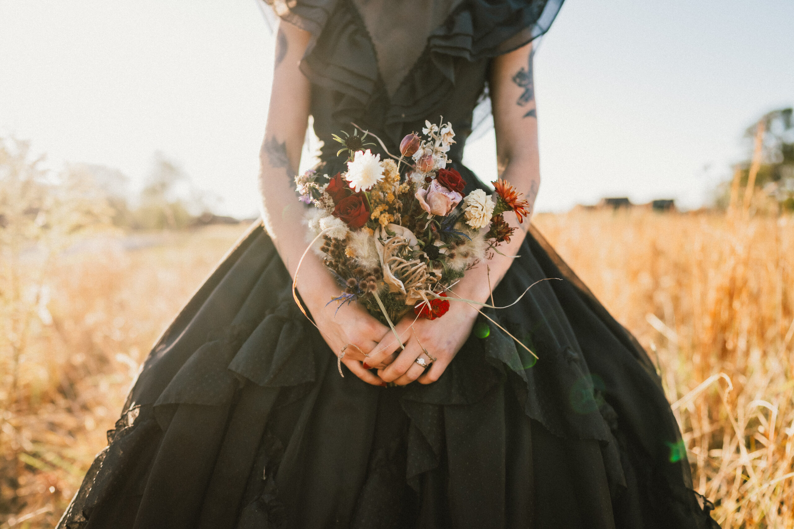 Erin & Baxter's day: Erin holds a dried bouquet in her ruffled black gown in golden grass at Covey Creek
