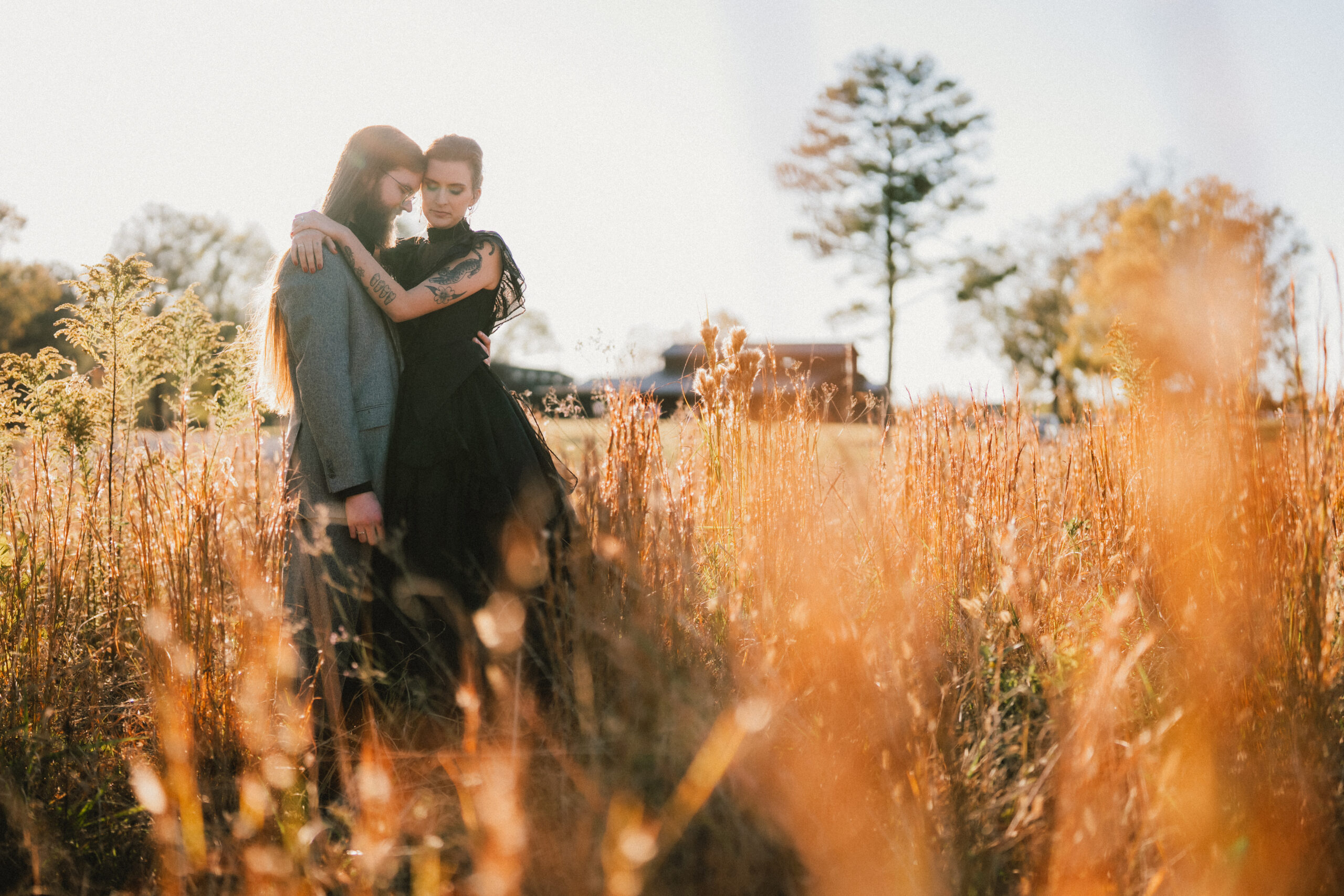 Erin & Baxter embrace forehead-to-forehead in tall golden grass with the barn at Covey Creek