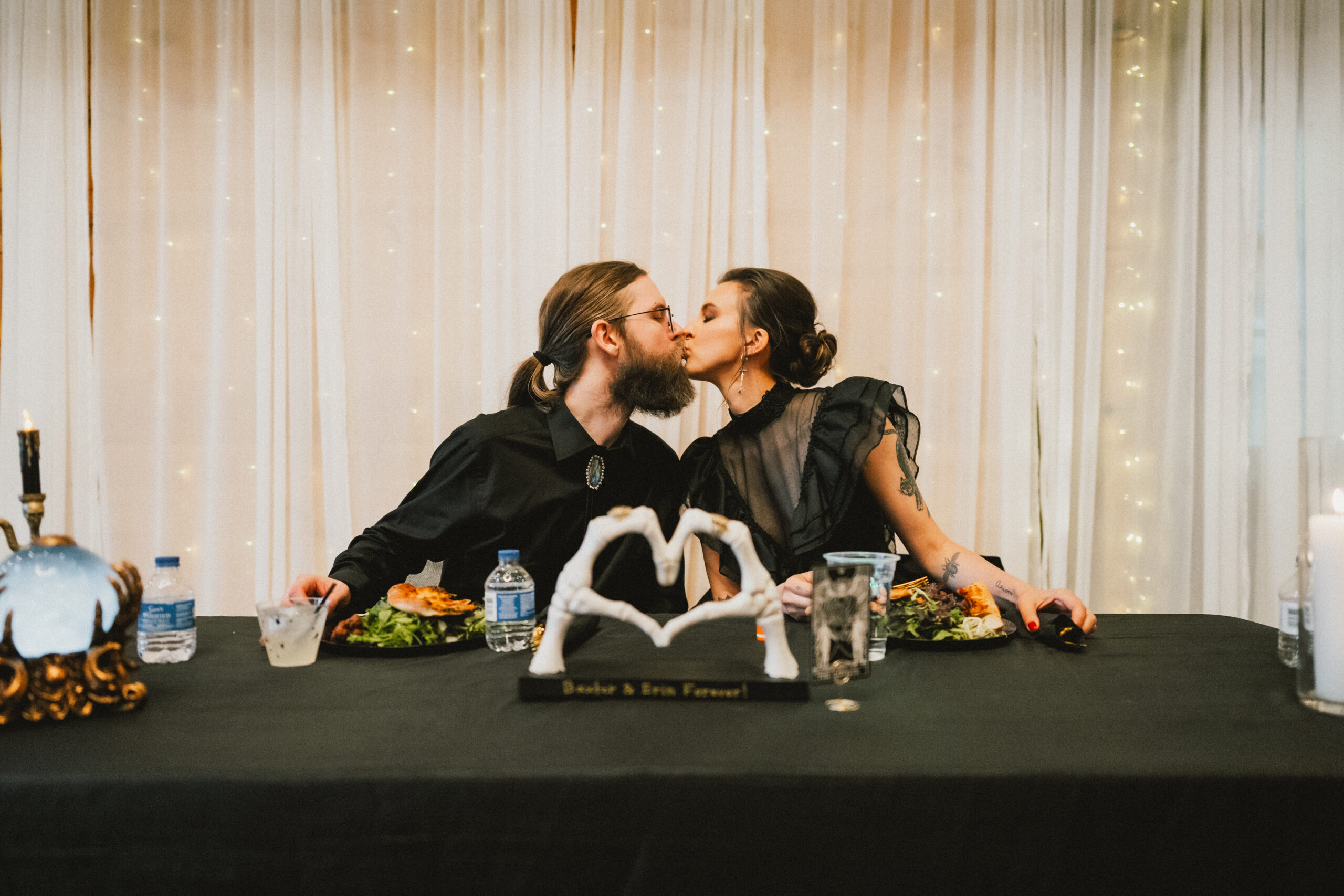 Erin & Baxter kiss at their sweetheart table with a skeleton-hand heart decor at Covey Creek