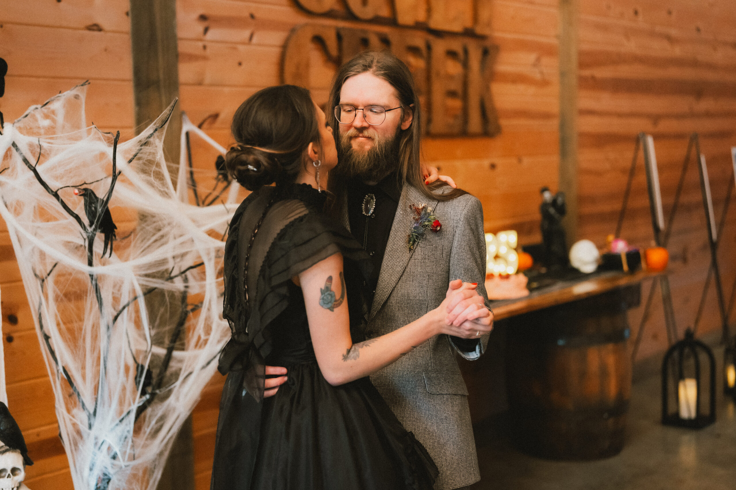 Erin & Baxter slow dance by the carved Covey Creek sign amid spiderwebs and Halloween decor in the barn