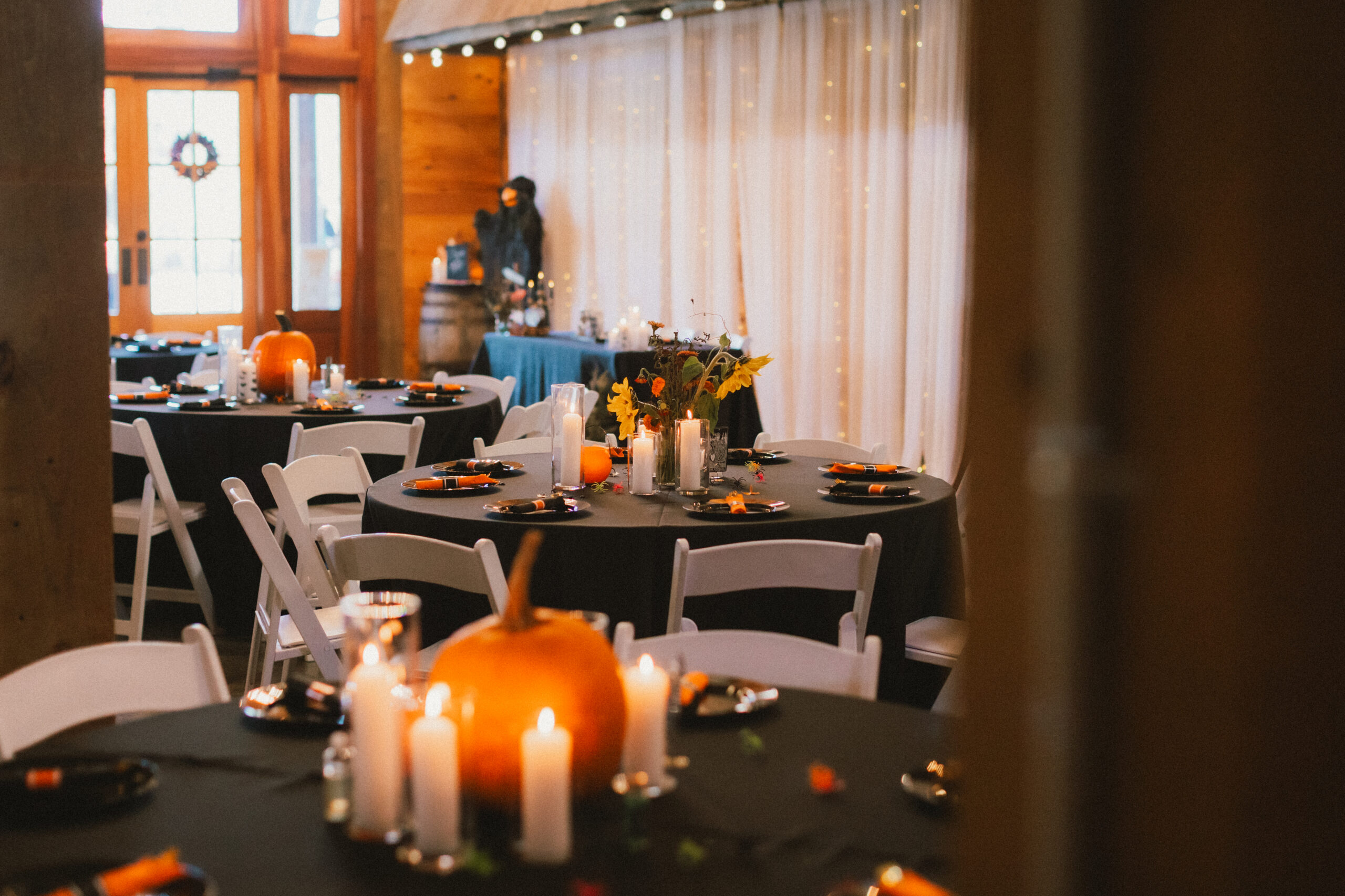 Black-clothed tables with pumpkin centerpieces and candlelight fill Erin & Baxter's barn at Covey Creek