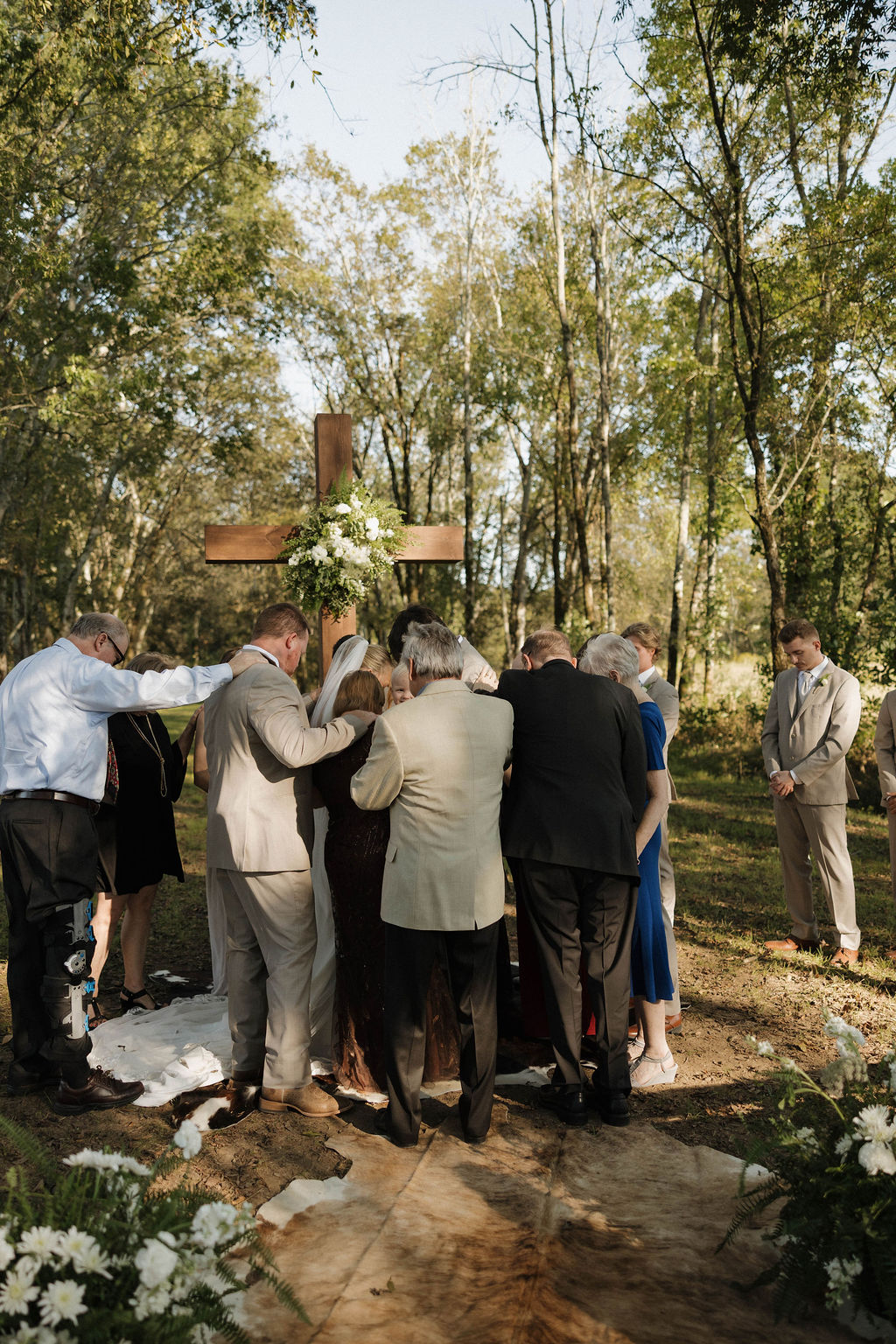 Wedding party prays over Hailey & Joseph before a flower-draped wooden cross at their Covey Creek ceremony
