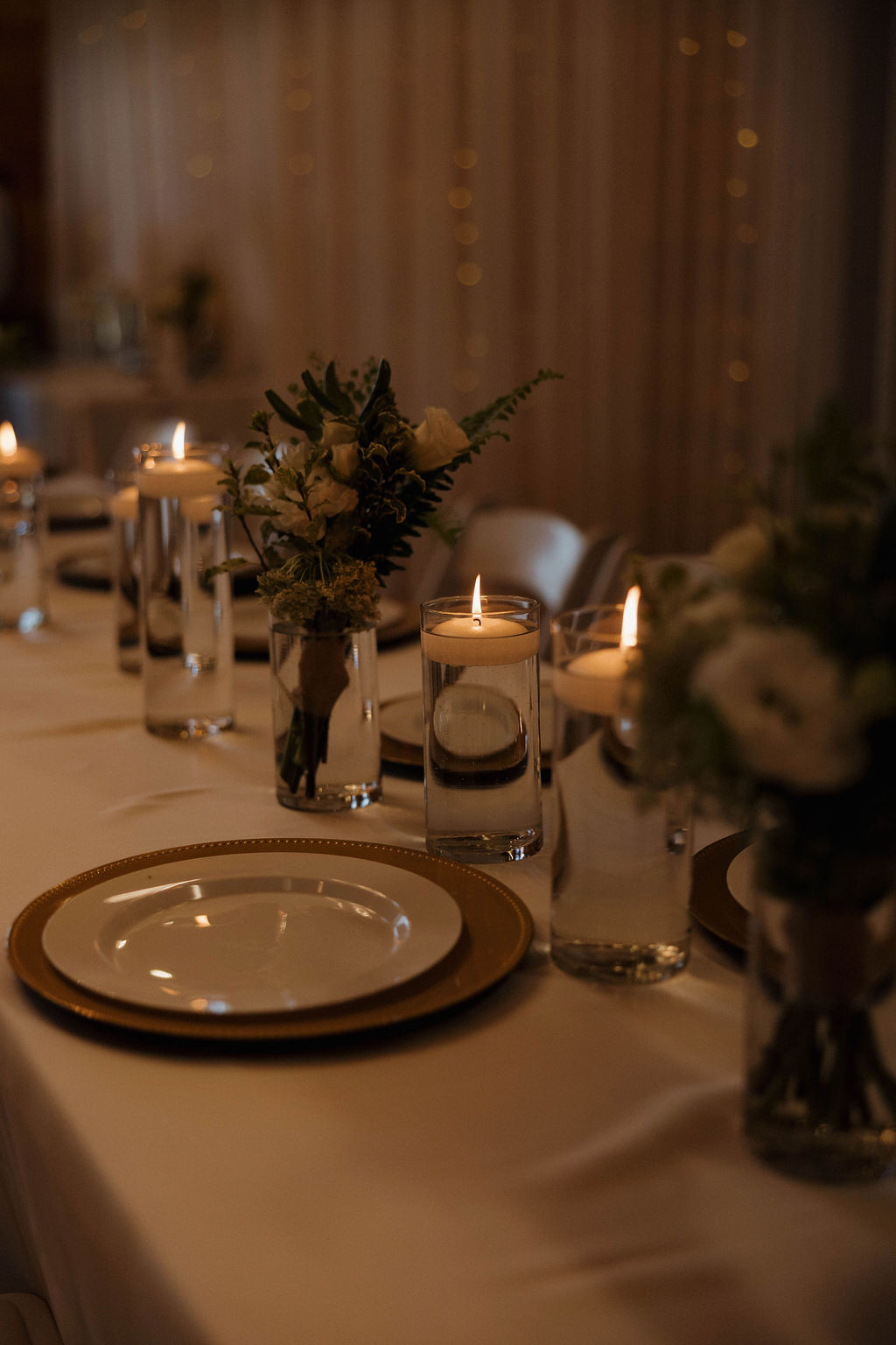 Gold charger, floating candles, and white florals on Hailey & Joseph's reception table at Covey Creek