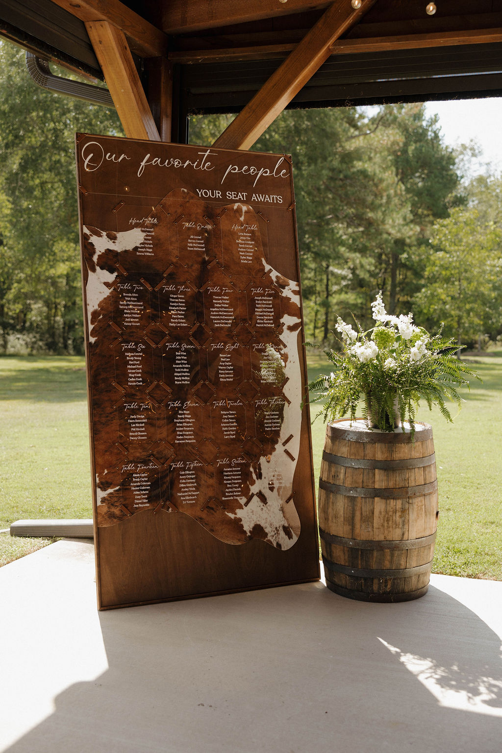 Hailey & Joseph cowhide seating chart on a wooden board beside barrel florals at the Covey Creek pavilion