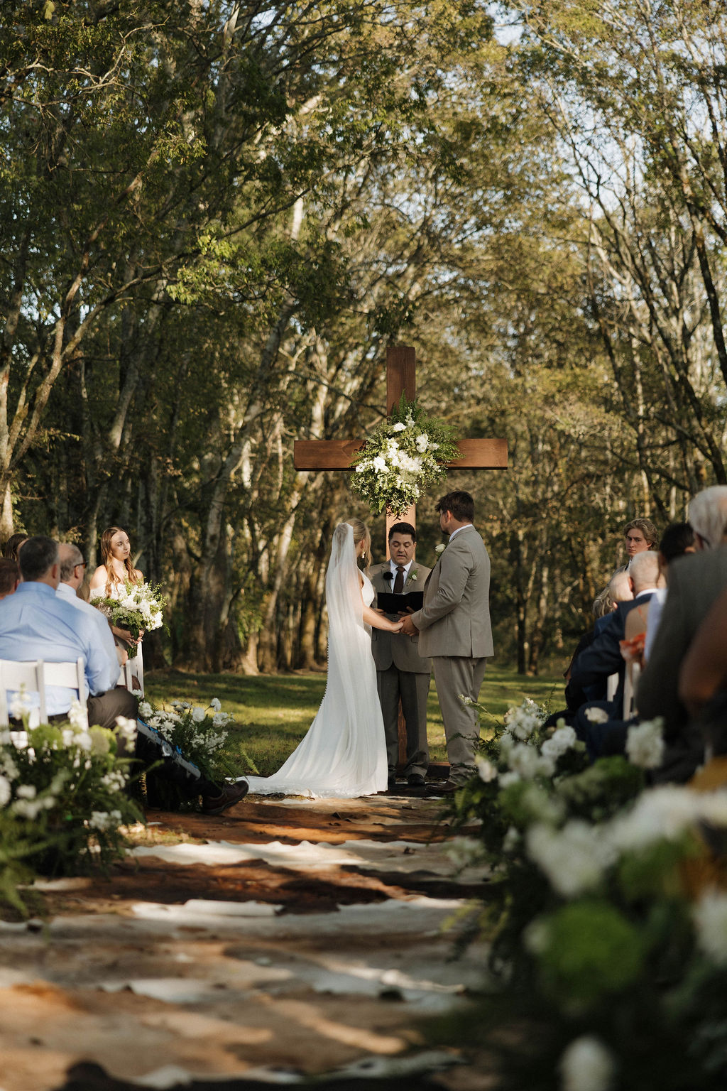 Hailey & Joseph exchange vows on a cowhide aisle before a floral wooden cross at Covey Creek