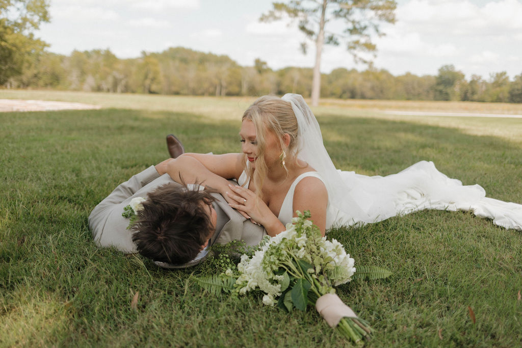 Hailey & Joseph lie in the grass with her white bouquet nearby during portraits at Covey Creek
