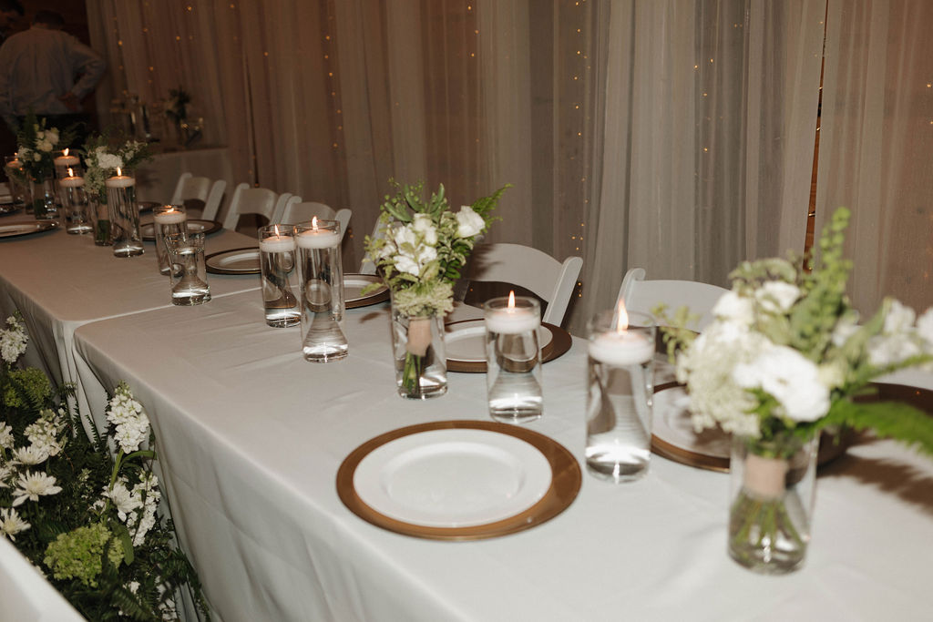 Hailey & Joseph head table with gold-rimmed plates, floating candles, and white florals at Covey Creek