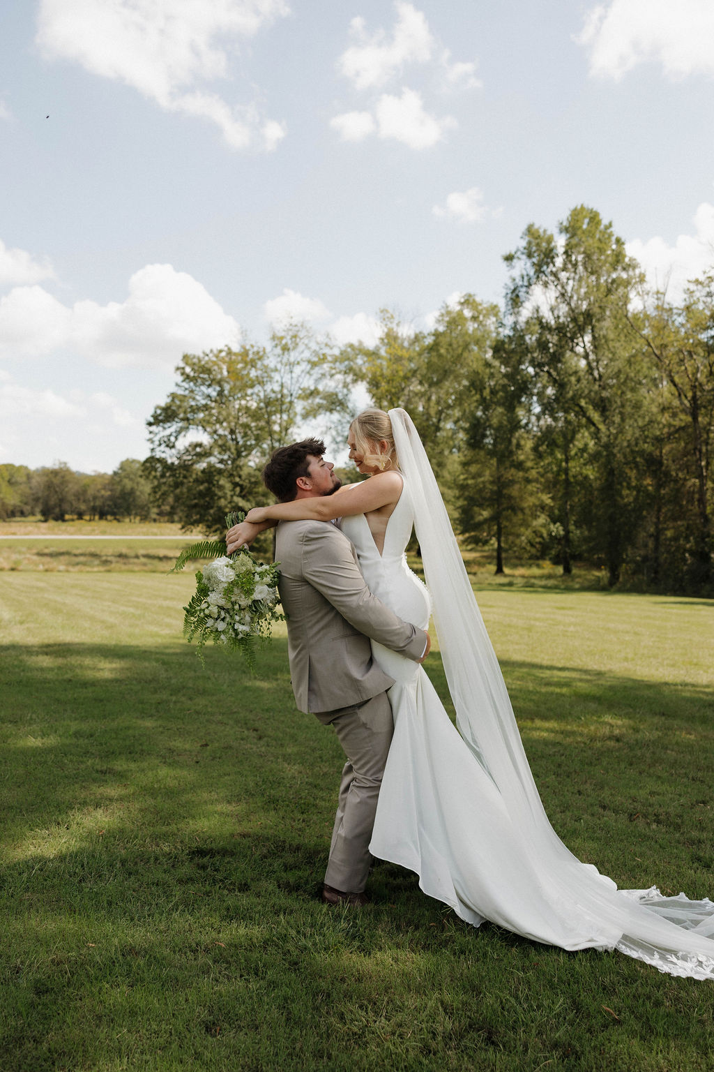 Joseph lifts Hailey in her white gown as they smile in a grassy field at Covey Creek for Hailey & Joseph