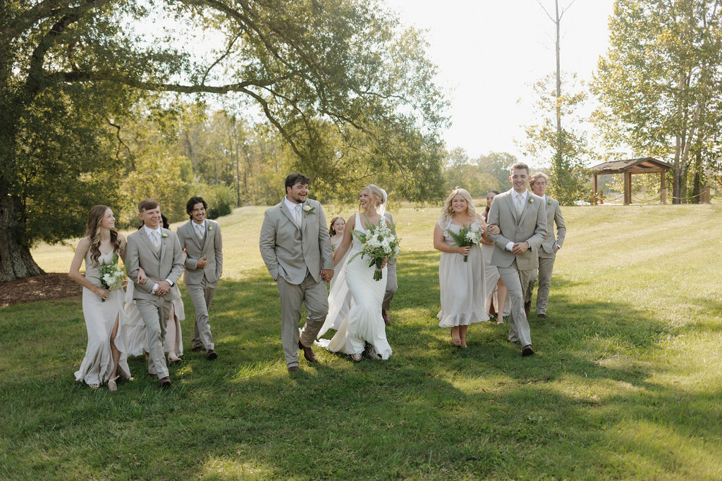 Hailey & Joseph walk with bridesmaids and groomsmen across the sunny lawn at Covey Creek wedding