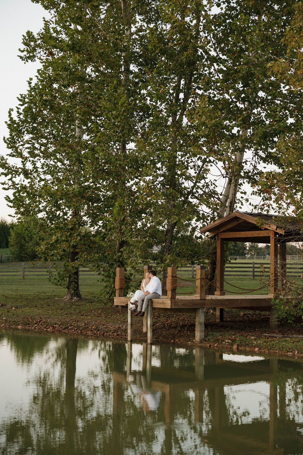 Hailey & Joseph sit on the Pond dock with their reflection visible in the water at Covey Creek