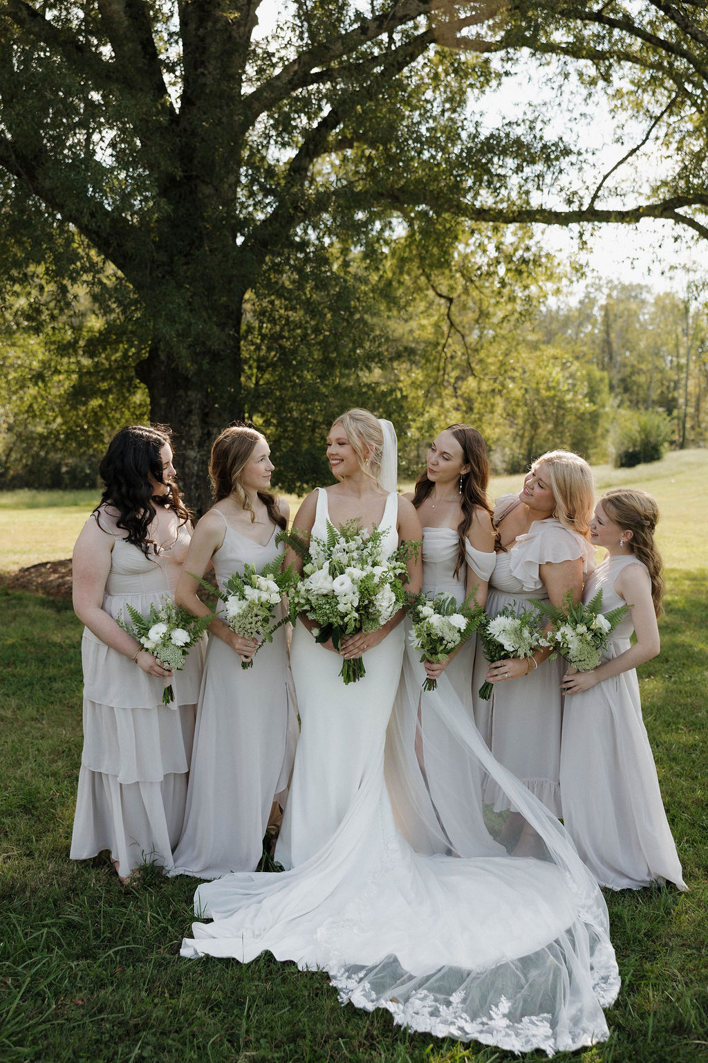 Hailey poses with bridesmaids in champagne gowns under a large tree on the Covey Creek lawn for Hailey & Joseph