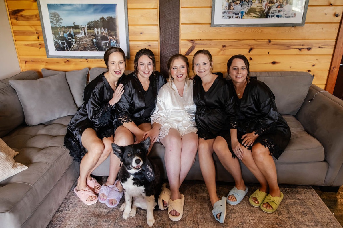Hannah and bridesmaids in satin robes pose on a grey sofa with their dog at Covey Creek, Hannah & Nicholas.