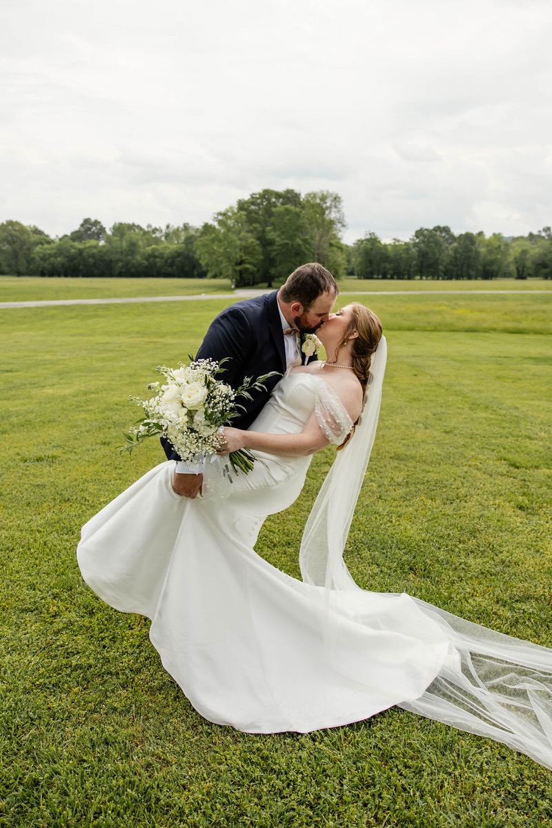 Nicholas dips Hannah for a kiss on Covey Creek's green lawn, white bouquet and veil trailing, Hannah & Nicholas.