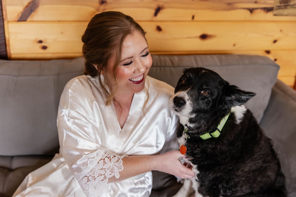Hannah in a lace satin robe cuddles her black-and-white dog on a grey sofa at Covey Creek, Hannah & Nicholas.