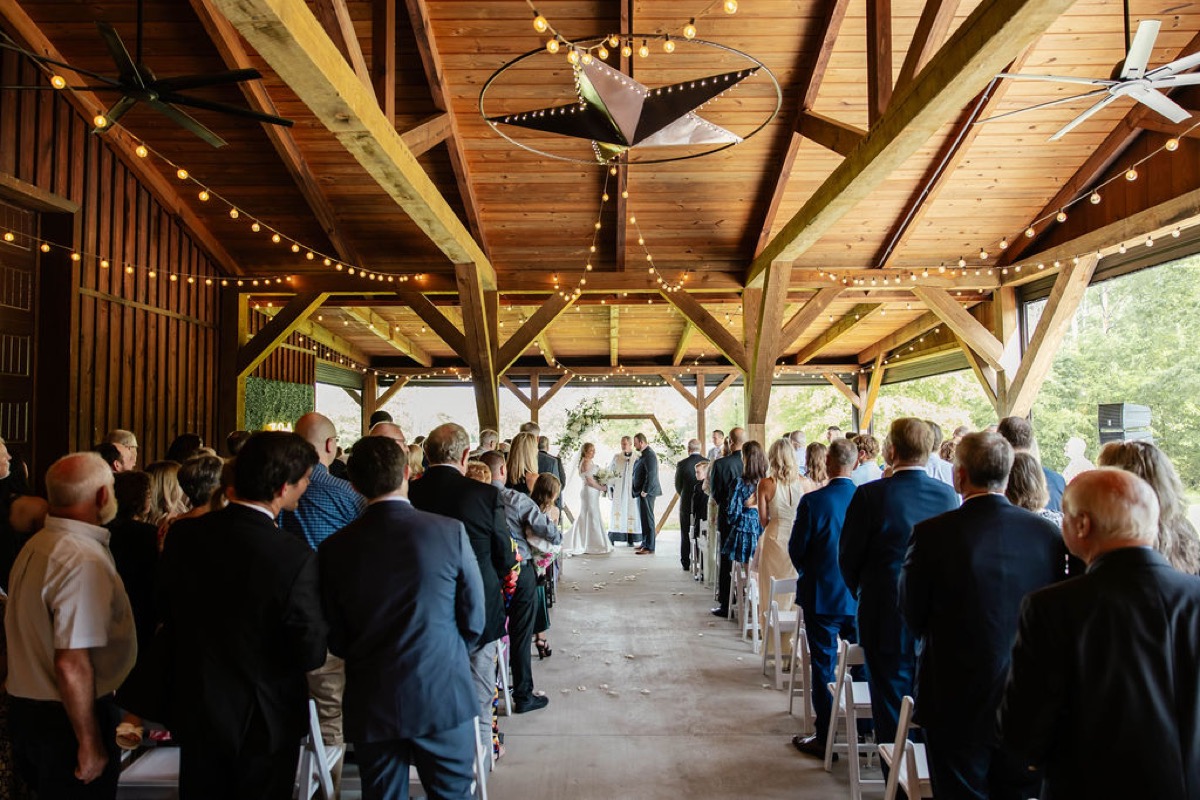 Wide view of Hannah & Nicholas exchanging vows under string lights in Covey Creek's timber pavilion.