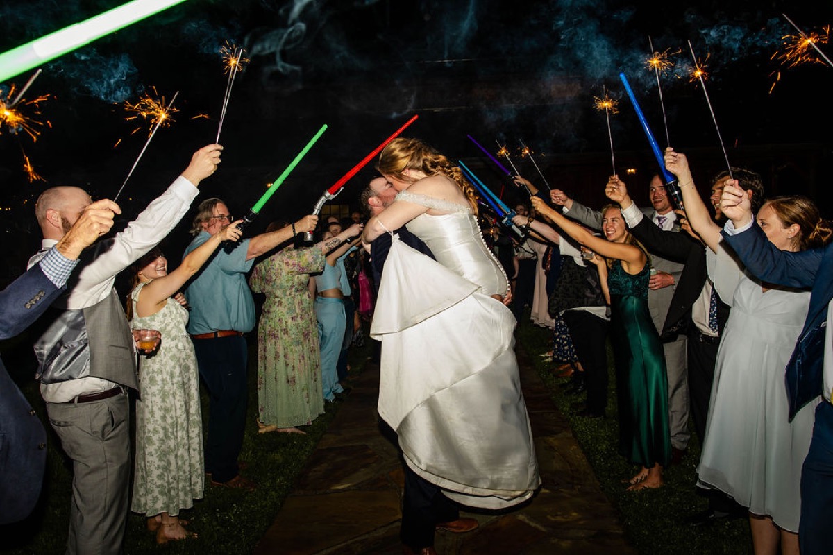 Nicholas lifts Hannah for a kiss through lightsabers and sparklers at their Covey Creek send-off, Hannah & Nicholas.