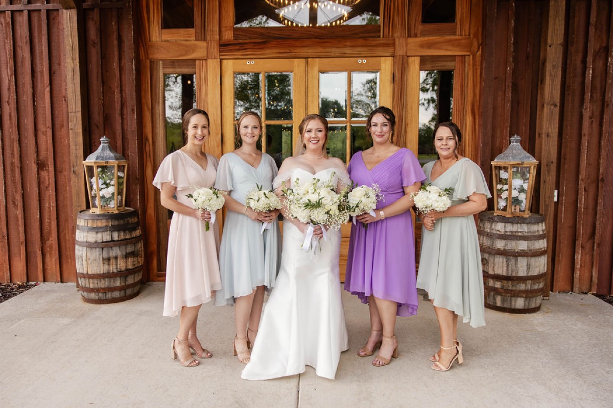Hannah and pastel bridesmaids pose with white bouquets by lantern barrels at Covey Creek, Hannah & Nicholas.