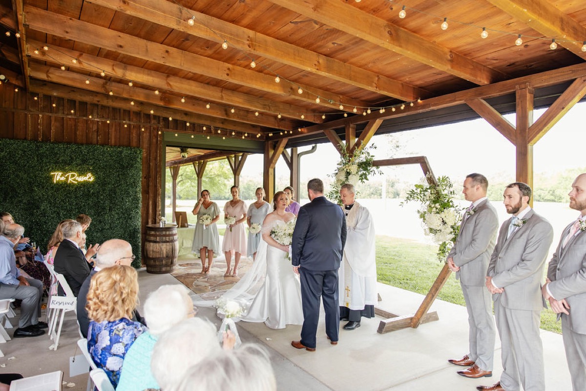 Hannah & Nicholas stand at the flowered hex arch with pastel bridal party at Covey Creek's pavilion.