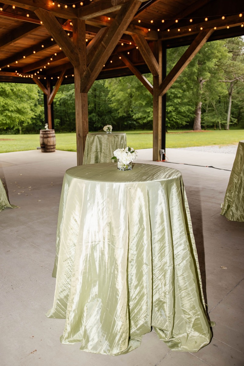 Sage cocktail tables with white florals under string lights in Covey Creek's pavilion for Hannah & Nicholas.
