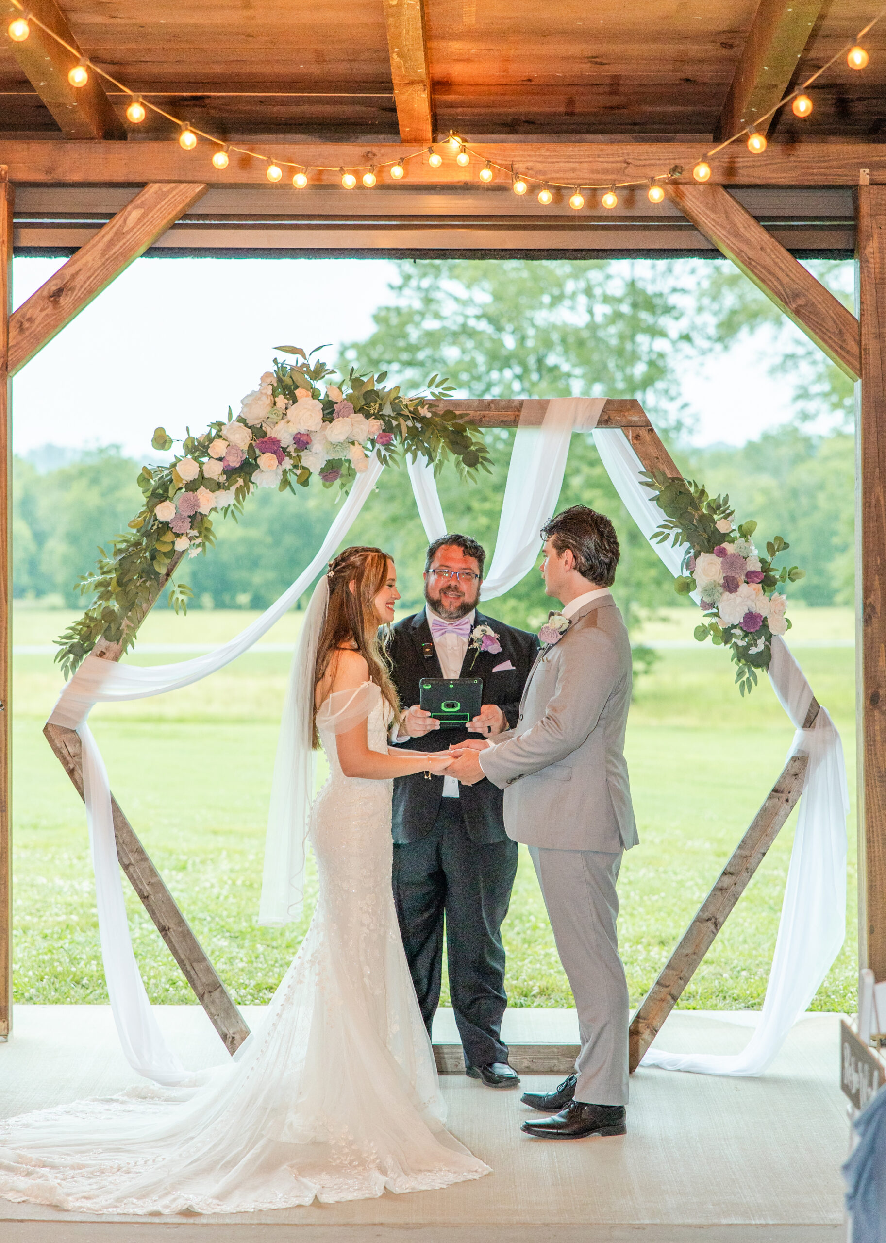 Hannah & Ryan hold hands under a floral hexagonal arch in the patio pavilion at Covey Creek.