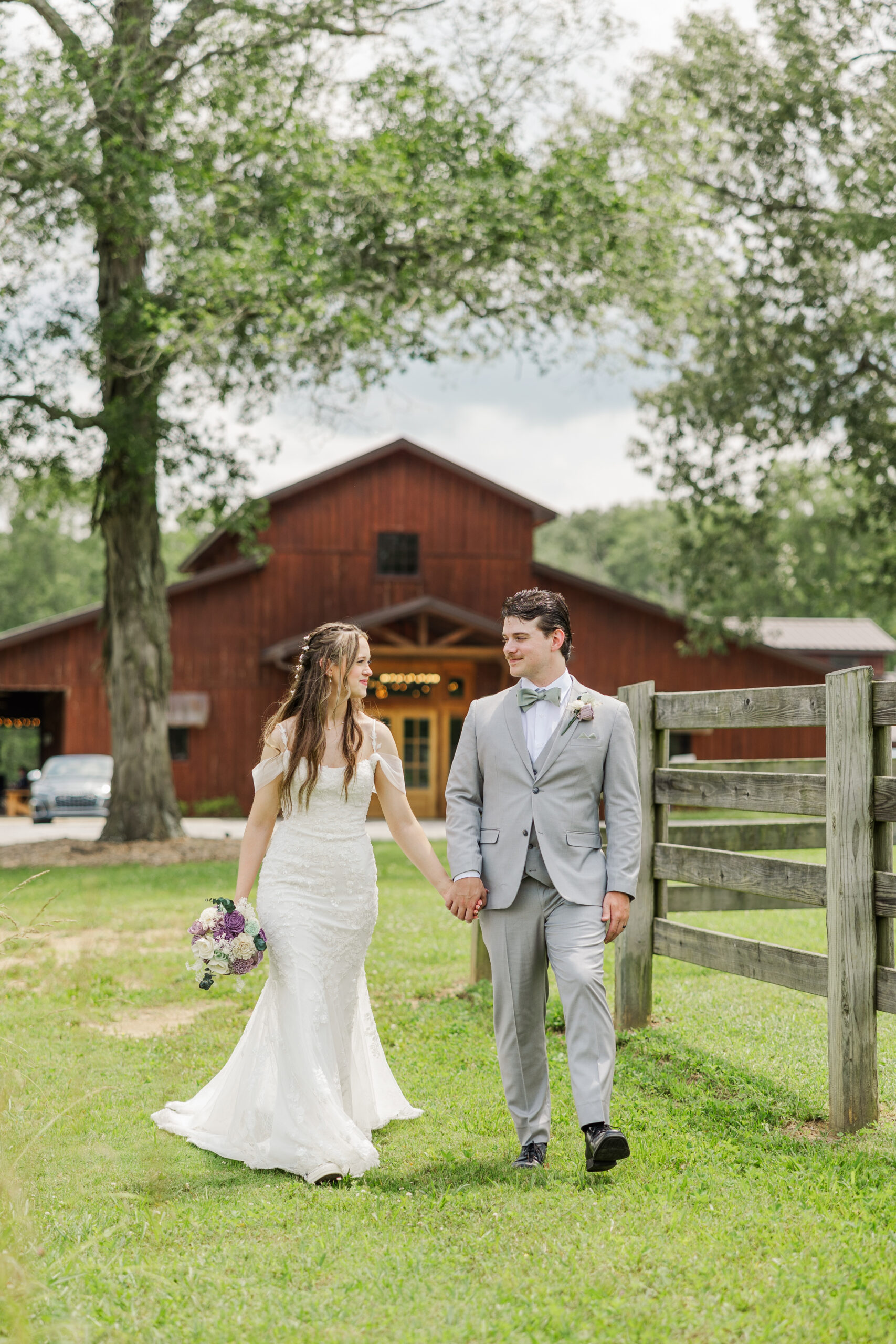 Hannah & Ryan walk hand-in-hand across the lawn before the rustic red barn at Covey Creek.