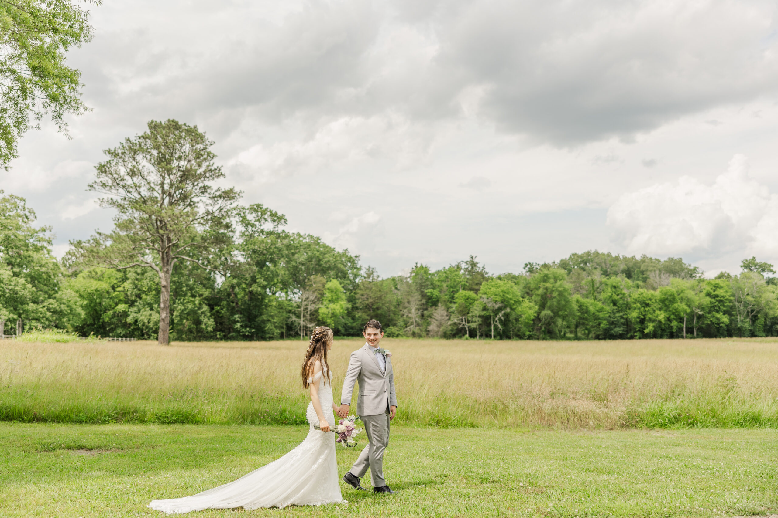 Hannah & Ryan walk a golden meadow, Ryan glancing back, under cloudy skies at Covey Creek.