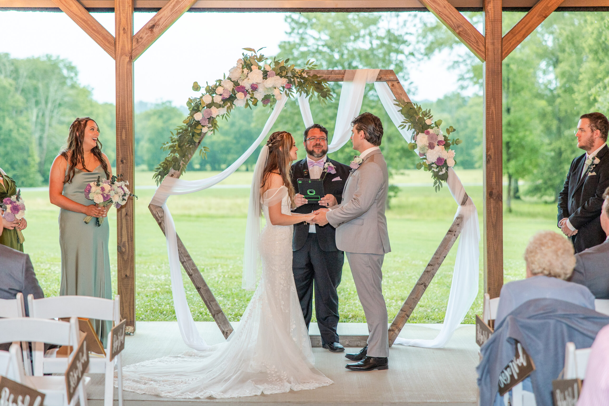 Hannah & Ryan exchange vows beneath a floral hexagonal arch in the patio pavilion at Covey Creek.