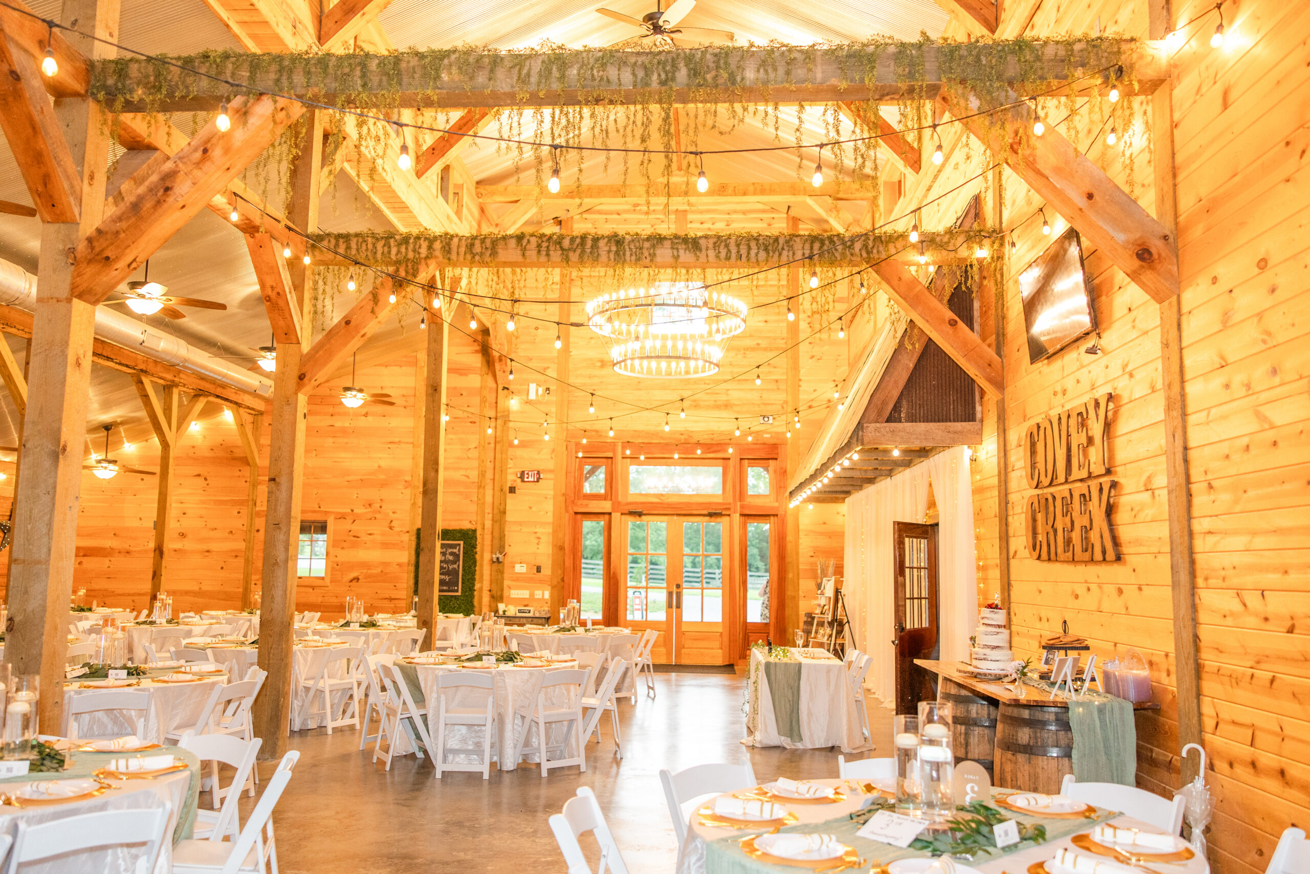 Covey Creek reception hall set for Hannah & Ryan with chandeliers, greenery, and wedding cake.