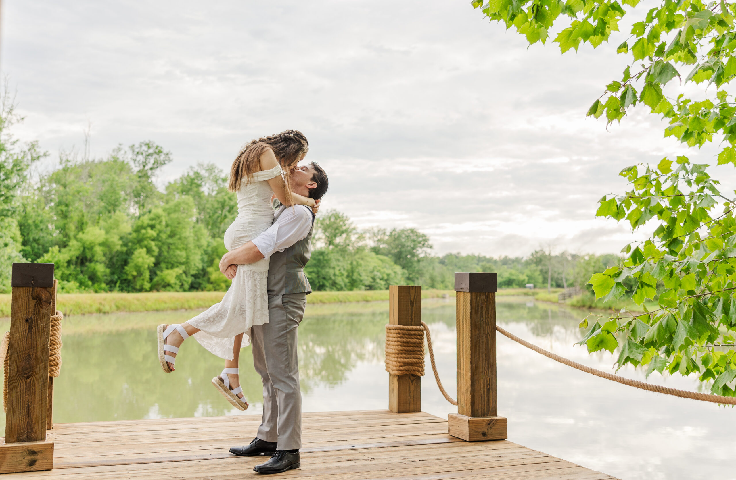 Ryan lifts Hannah for a kiss on the pond dock overlooking calm still water at Covey Creek.
