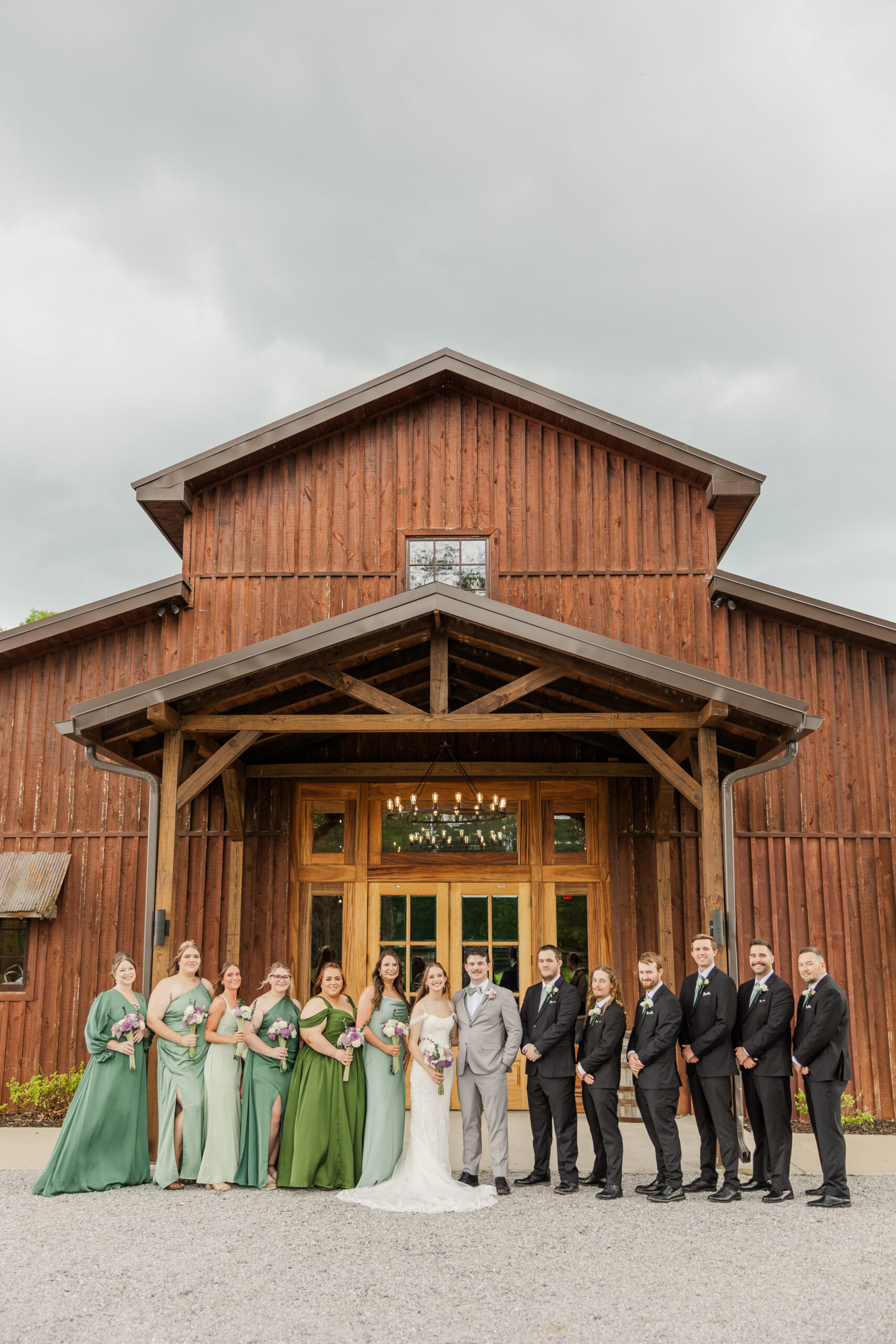 Hannah & Ryan pose with their bridal party in sage and black before the barn at Covey Creek.