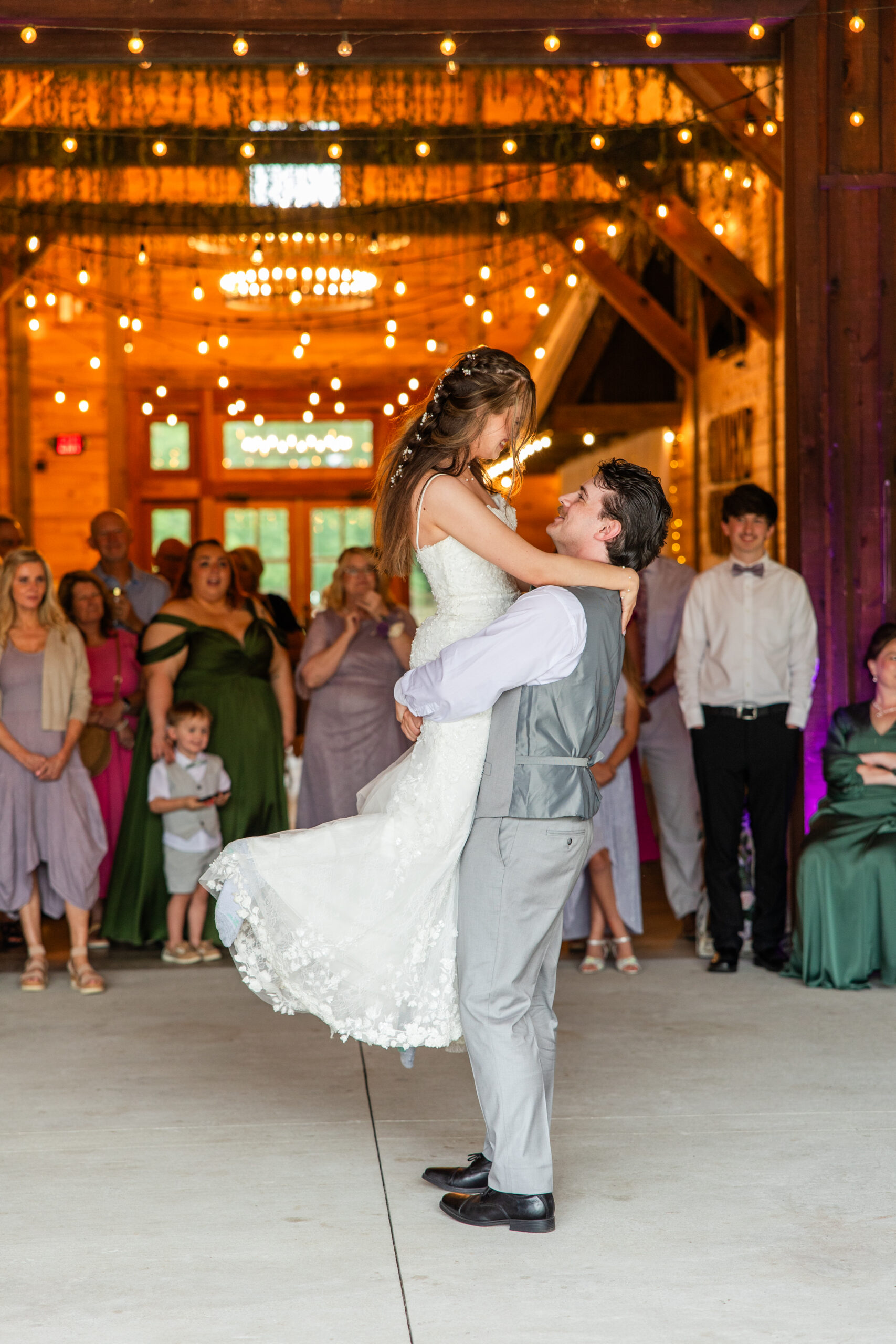 Ryan lifts Hannah mid-dance under warm string lights in the reception barn at Covey Creek.