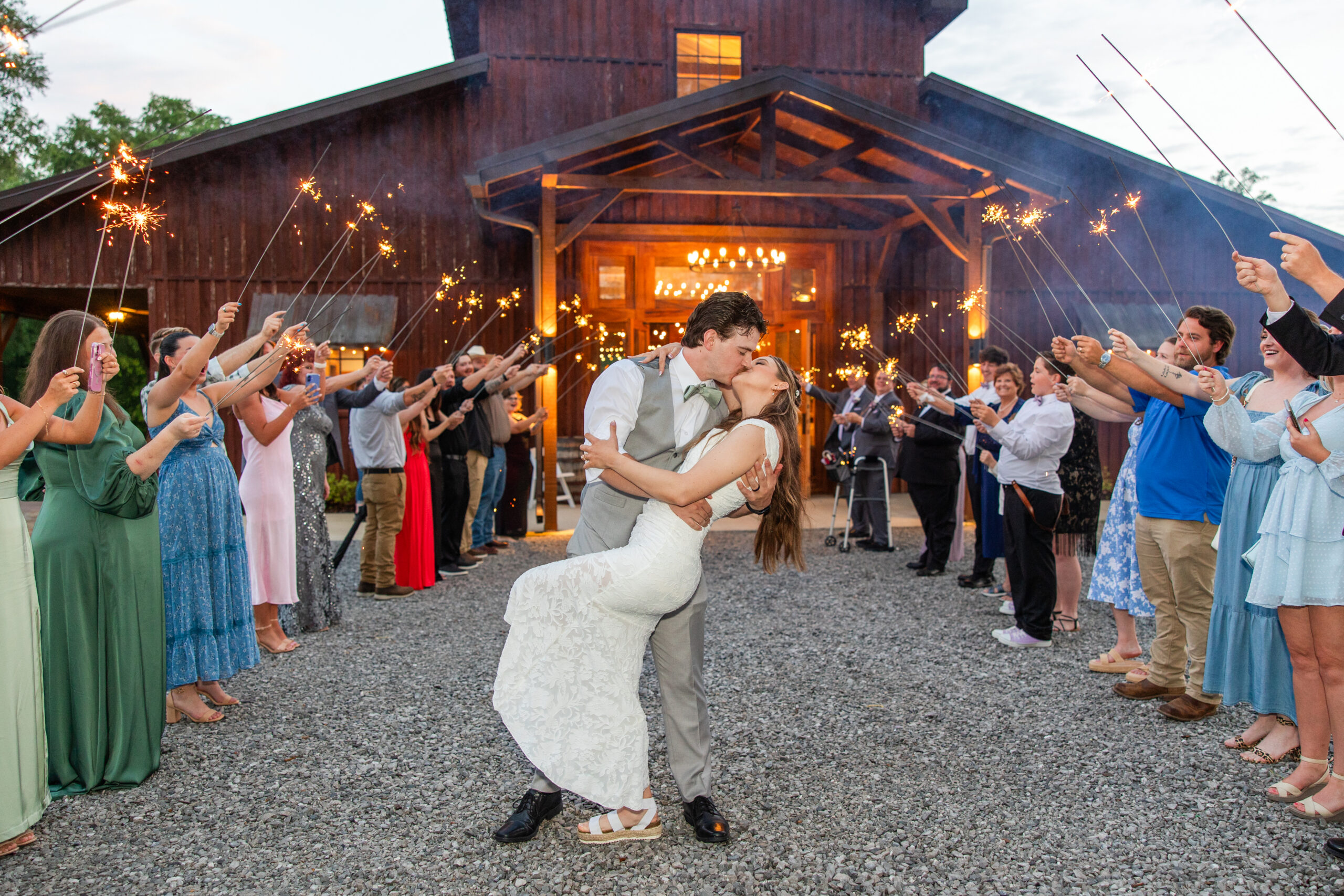Hannah & Ryan kiss amid lit guest sparklers outside the barn entrance at dusk at Covey Creek.