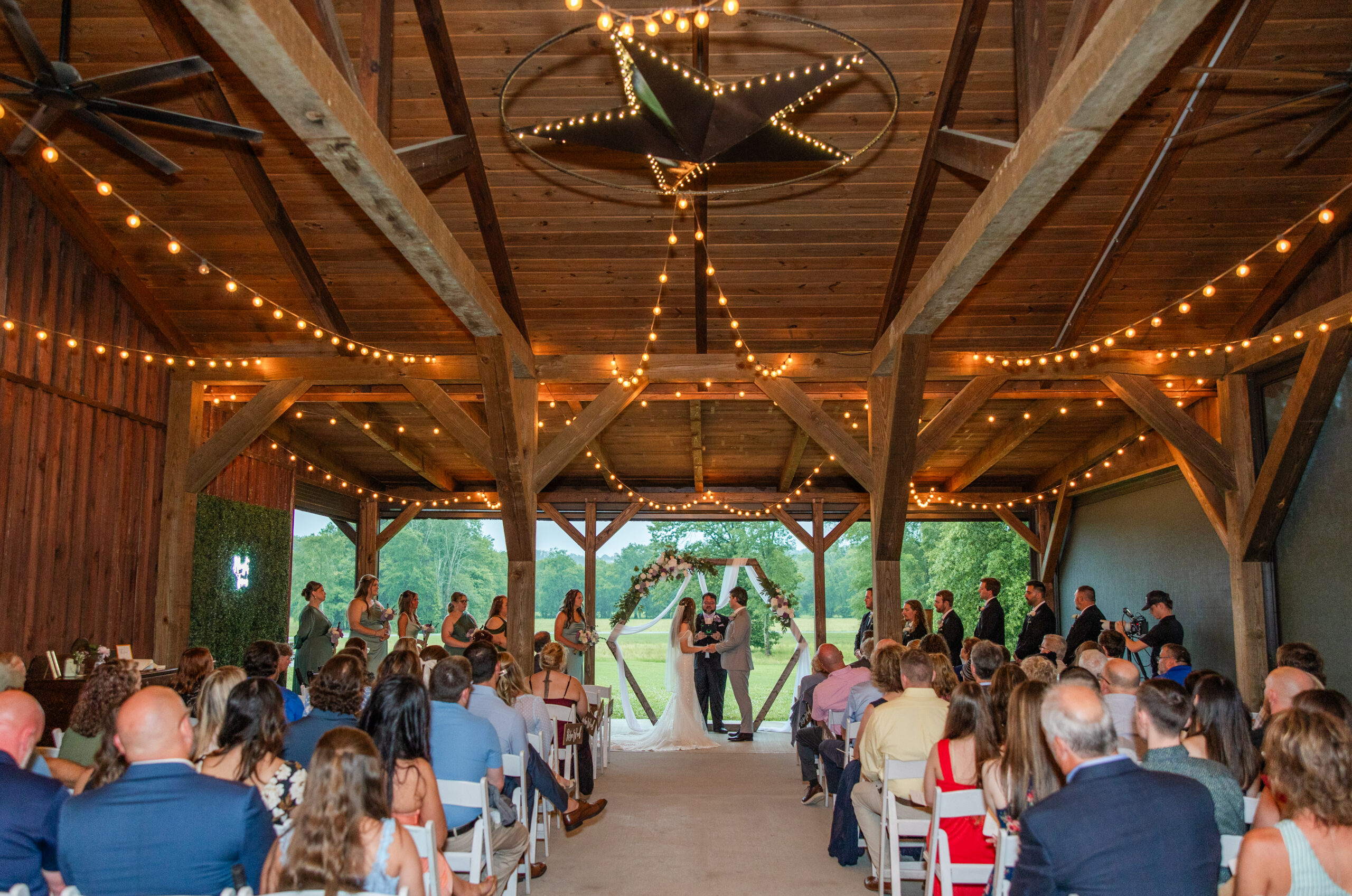 Hannah & Ryan stand at the hexagonal arch as guests fill the string-lit pavilion at Covey Creek.