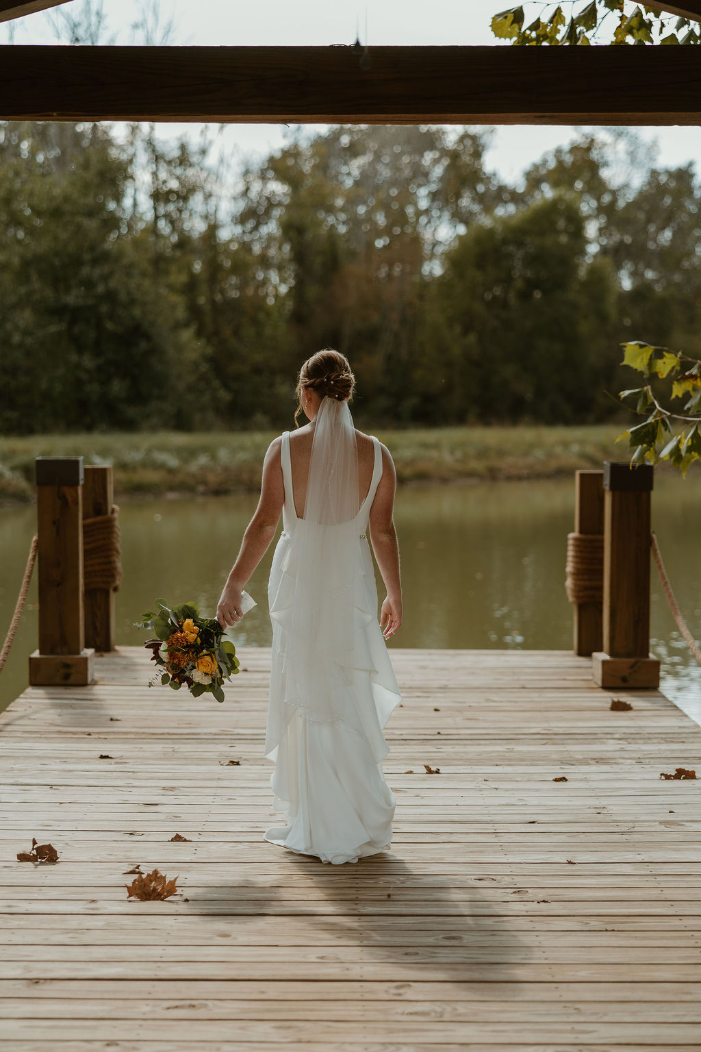 JJ & Will: bride JJ in a low-back gown and veil stands on the Pond dock overlooking water at Covey Creek