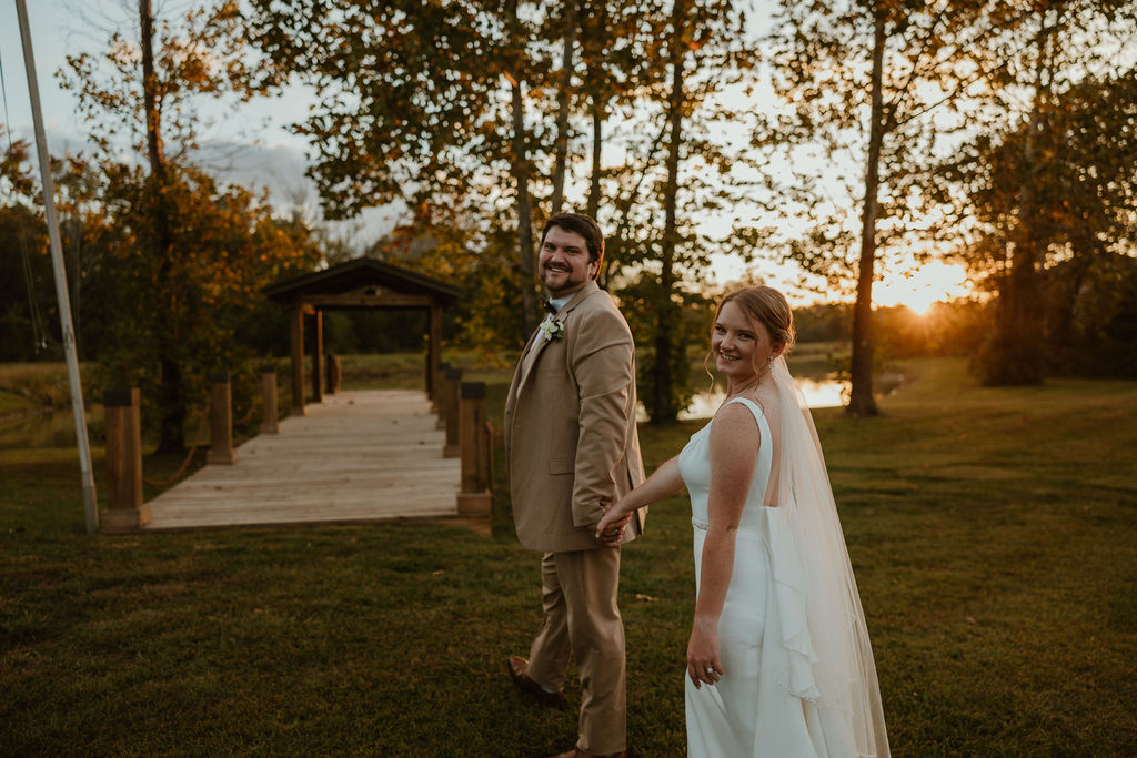 JJ & Will look back smiling while walking the lawn by the Pond pavilion at sunset at Covey Creek