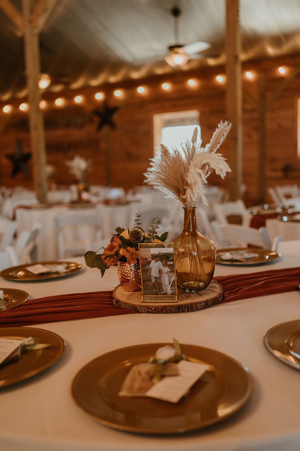 JJ & Will reception centerpiece with pampas, orange florals, and framed photo indoors at Covey Creek