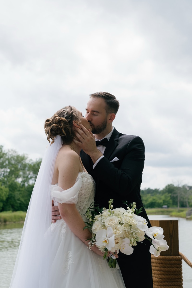 Katelyn & Josh kiss on Covey Creek’s Pond dock, her orchid bouquet and rope-wrapped post in frame