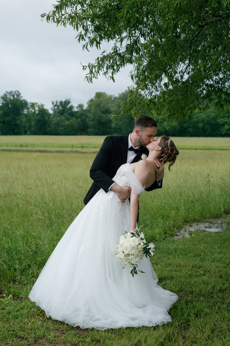Katelyn & Josh share a dip kiss on Covey Creek’s lawn, her white orchid bouquet trailing toward the grass